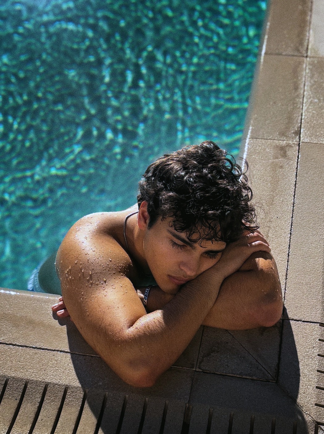 Portrait of a man resting his arms on the edge of a sunlit turquoise swimming pool