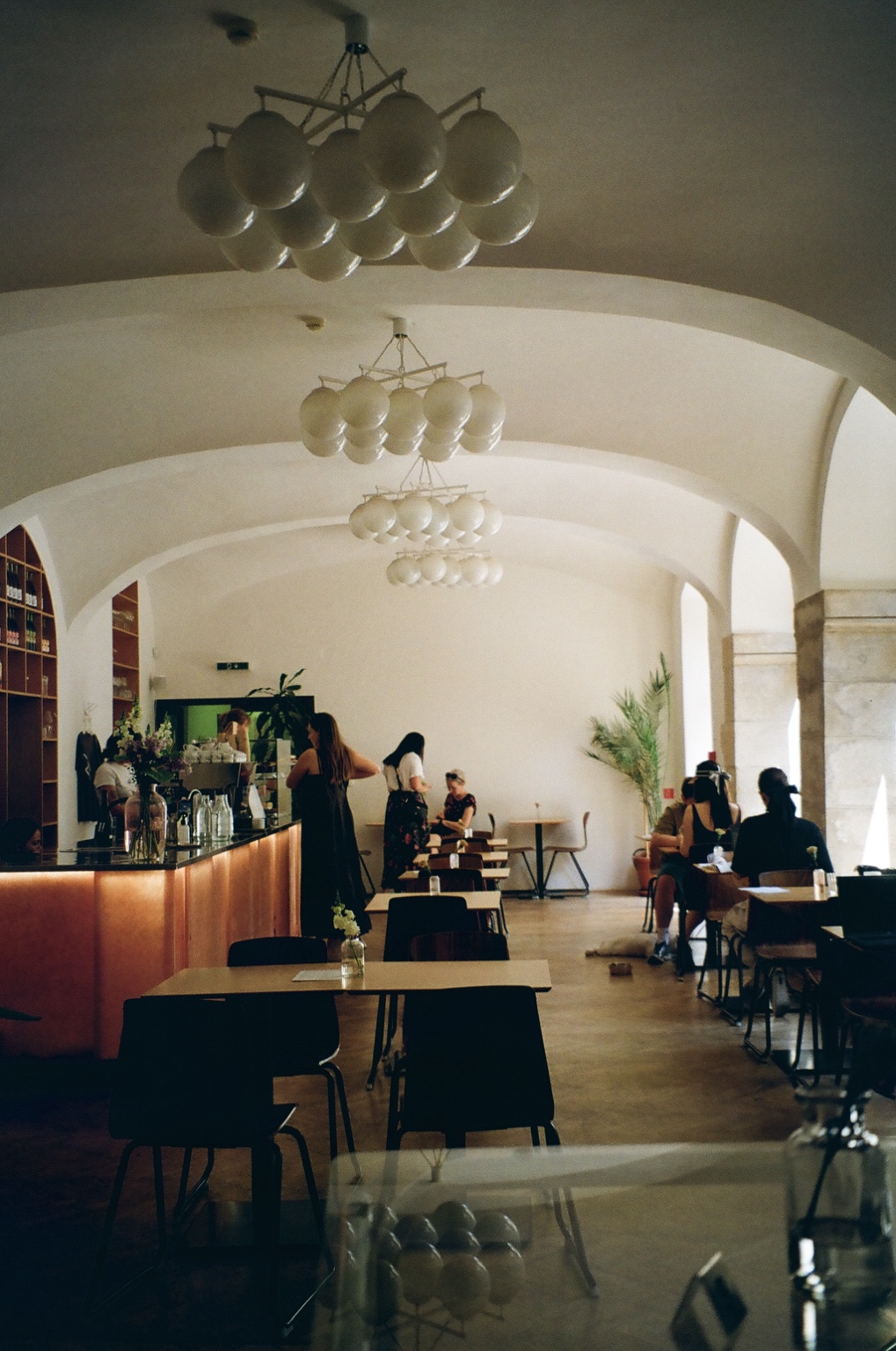Sunlit café interior with arched ceilings and globe chandeliers